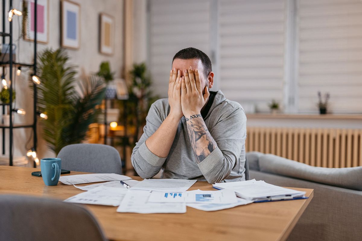 Stressed man covering his face with both hands and going through his bills and financial reports.
 (Getty Images/urbazon)